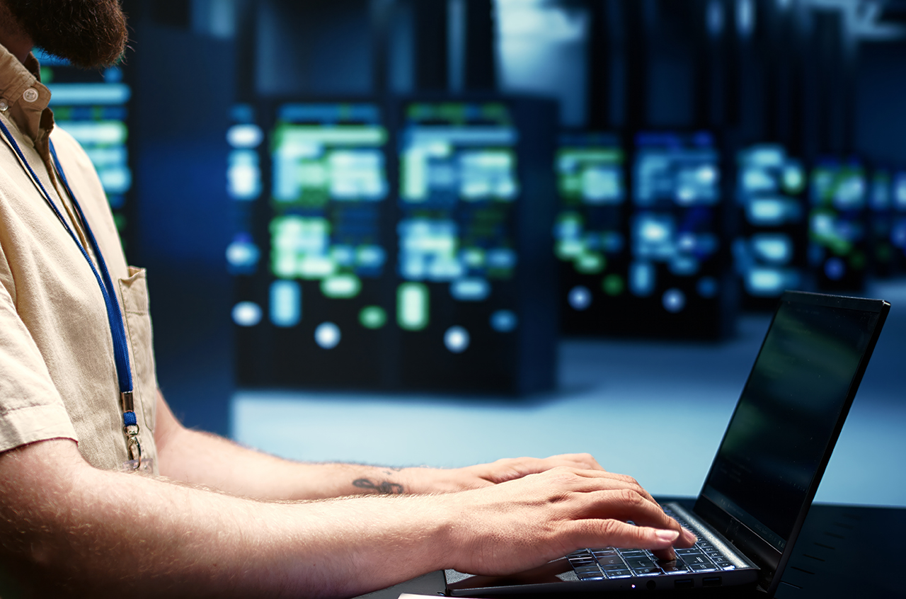 Supervisor running blade servers diagnostic tests and bug checking utilities to determine and repair software issues. Technician using laptop to survey critical systems, checking for flaws, close up